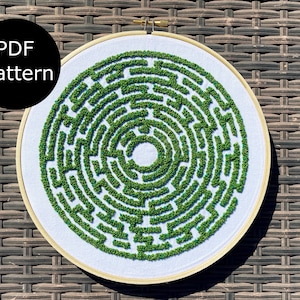 May include: A white embroidery hoop with a green and white circular maze pattern. The pattern is made of small green stitches that resemble a forest.