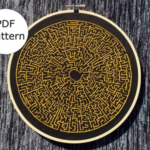 May include: A black embroidery hoop with a gold embroidered maze pattern. The pattern is a circular maze with a centre hole. The hoop is on a grey textured surface. PDF pattern.