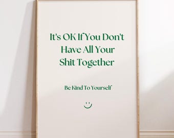 May include: A framed poster with the text "It's OK If You Don't Have All Your Shit Together" in green font. Below, it reads "Be Kind To Yourself" and a smiling face. The poster is on a wooden floor.