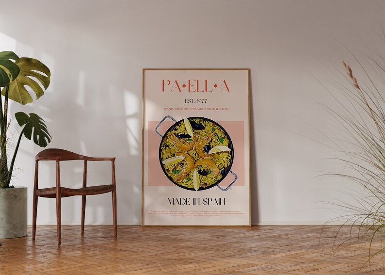 May include: A framed poster with a pink background and a photo of a paella dish with shrimp, mussels, and lemon wedges. The poster has the text "PAELLA" in a red font and "EST. 1977" in a smaller font. The text "MADE IN SPAIN" is at the bottom of the poster.