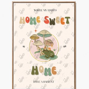May include: A framed art print with a whimsical design. The artwork features the words "HOME SWEET HOME" in colorful, retro-style lettering, along with illustrations of mushrooms and a frog. The background has a repeating pattern of hand-like shapes.