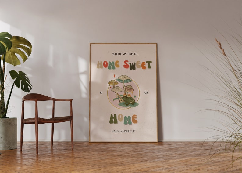 May include: A framed poster with the words "HOME SWEET HOME" in colorful, retro-style lettering. The poster features an illustration of mushrooms and a frog. The text "WHERE MY HABITS HAVE A HABITAT" is also included.