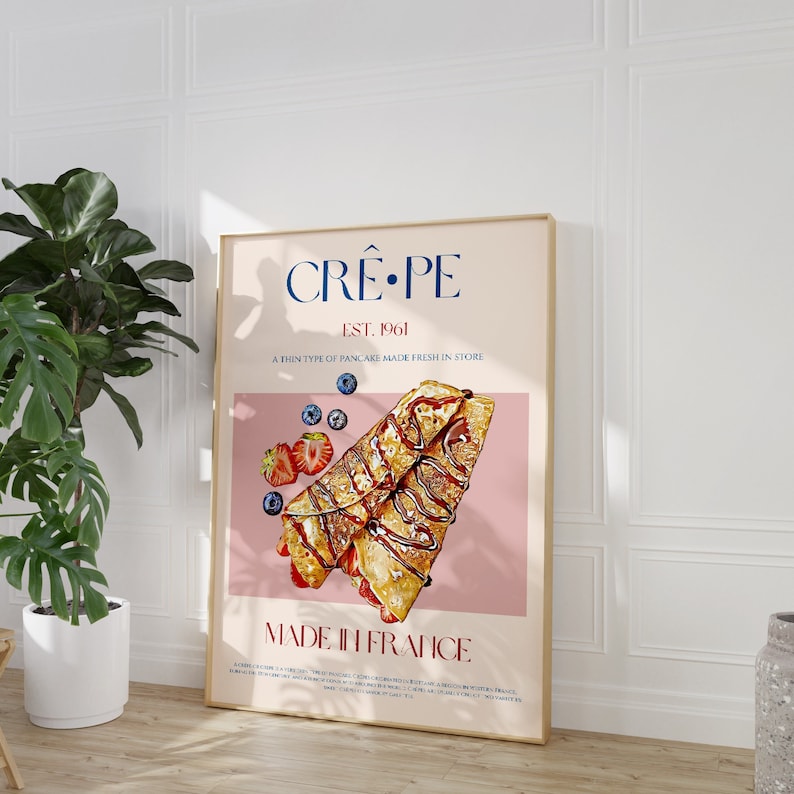 Op de afbeelding: Een roze en witte poster met de tekst "CR&Ecirc;PE EST. 1961 A THIN TYPE OF PANCAKE MADE FRESH IN STORE MADE IN FRANCE". De poster toont een illustratie van twee cr&ecirc;pes met chocoladesaus, aardbeien en blauwe bessen.