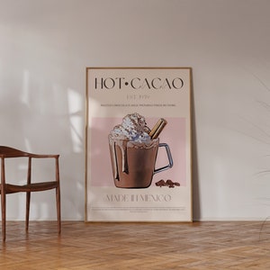 May include: A framed poster with a pink background and a graphic of a hot chocolate drink with whipped cream and a cinnamon stick. The text on the poster reads "HOT CACAO EST. 1991" and "MADE IN MEXICO".