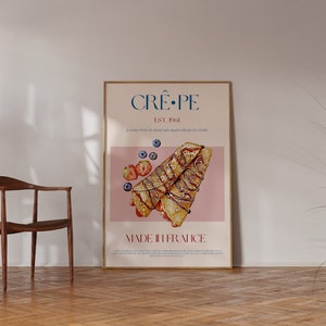 Op de afbeelding: Een poster met een roze achtergrond waarop een afbeelding van een cr&ecirc;pe met chocolade- en aardbeienvulling staat. De tekst op de poster luidt "Cr&ecirc;&middot;pe Est. 1961 Een dun soort pannenkoek gemaakt van vers beslag Gemaakt in Frankrijk."