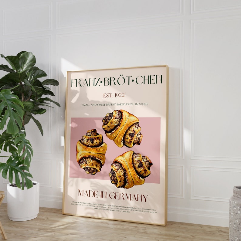 May include: A poster with a pink background featuring the text "Franz Br&ouml;t Chen" and "Est. 1922" in a green font. The poster also includes the text "Small and Sweet Pastry Baked Fresh in Store" and "Made in Germany". The poster features three cinnamon rolls with a brown and white swirl pattern.