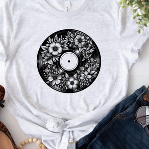 May include: A white t-shirt with a black and white graphic of a vinyl record with floral designs.
