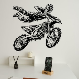 May include: Black and white silhouette of a motocross rider performing a trick on a dirt bike. The rider is in mid-air, with the bike's front wheel raised. The rider is wearing a helmet and goggles.