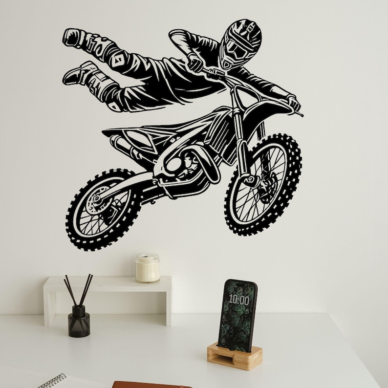 May include: Black and white silhouette of a motocross rider performing a trick on a dirt bike. The rider is in mid-air, with the bike's front wheel raised. The rider is wearing a helmet and goggles.