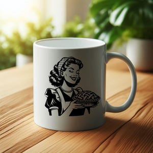 May include: White ceramic mug with a black and white illustration of a woman holding a pie. The woman is wearing a headband and an apron.