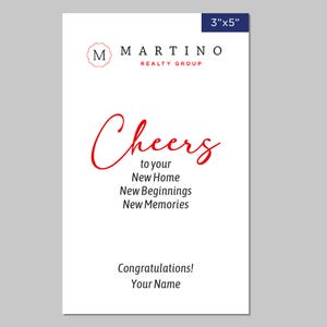 May include: A white card with red text that says "Cheers to your New Home, New Beginnings, New Memories". The card also has a logo for Martino Realty Group and the text "Congratulations! Your Name".