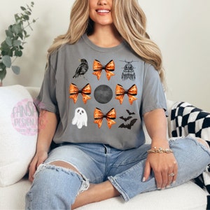 May include: A gray t-shirt with a black bird, bats, a ghost, and orange and white polka dot bows. The bows are arranged in a circle around a black circle.