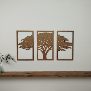 Könnte beinhalten: Drei Wandpaneele aus Holz mit Baumdarstellungen. Jedes Paneel zeigt ein Baumdesign, das aus Holz geschnitten und in einem rechteckigen Rahmen eingefasst ist. Die Bäume sind warmbraun, der Hintergrund ist weiß.