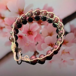 May include: A silver wire wrapped bracelet with pink and red gemstone beads.
