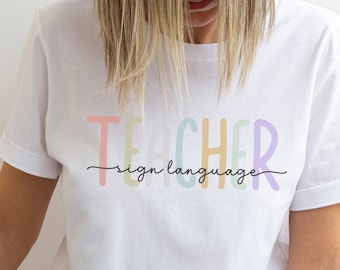 Może przedstawiać: Biała koszulka z napisem "TEACHER sign language" w kolorach tęczy.