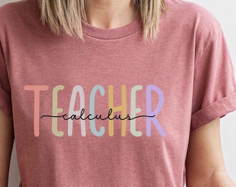Może przedstawiać: Różowy T-shirt z napisem "TEACHER" w kolorach tęczy i słowem "calculus" napisanym czarnym kolorem poniżej.