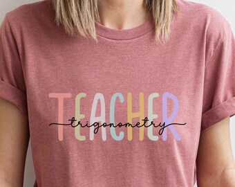 Może przedstawiać: Różowy T-shirt z napisem "TEACHER" w kolorach tęczy i napisem "trigonometry" w kolorze czarnym poniżej.