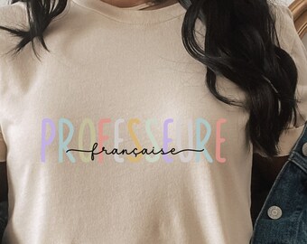 Może przedstawiać: Jasnobeżowy t-shirt z napisem "PROFESSEURE française" w kolorach tęczy.