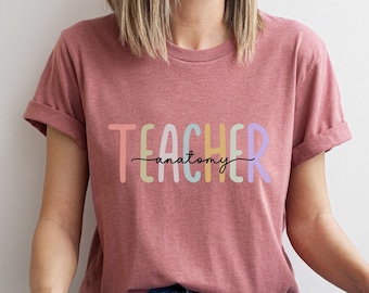 Może przedstawiać: Różowy T-shirt z napisem "TEACHER anatomy" w kolorach tęczy.