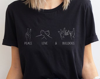 May include: Black t-shirt with white text and illustrations of hands signing "peace", "love", and "bulldogs".