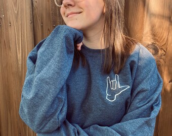May include: A dark blue sweatshirt with a white outline of the American Sign Language symbol for "I love you" on the front.