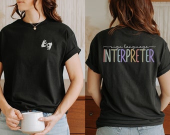 May include: Black t-shirt with a sign language hand symbol on the front and the text "sign language interpreter" in rainbow colors on the back.