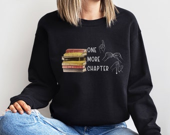 May include: Black sweatshirt with a stack of books and the text "ONE MORE CHAPTER" in white. The text is accompanied by hand gestures in sign language.