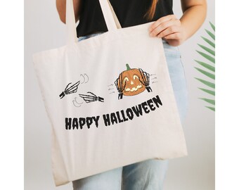 May include: A white tote bag with a black and orange Halloween design. The design features a pumpkin with hands covering its eyes and the text "Happy Halloween".