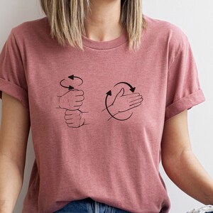 May include: A heather pink t-shirt with a graphic of two hands demonstrating the ASL sign for "I love you".