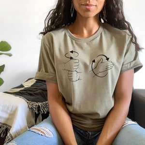 May include: A person wearing a green short-sleeved t-shirt with a black graphic of two hands signing the word "love" in American Sign Language.