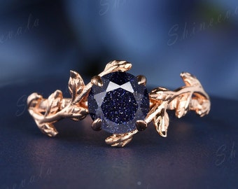 Könnte beinhalten: Ein Ring aus Roségold mit einem blauen Edelstein, der von Blattdetails umgeben ist.