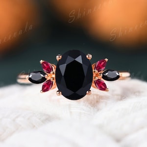 May include: A rose gold ring with a black oval gemstone surrounded by smaller red and black gemstones.