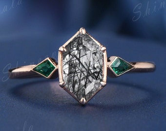 May include: A rose gold ring with a hexagonal black and white gemstone and two emerald green accent stones.