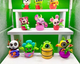 May include: A collection of colorful character figurines displayed on white shelves against a green backdrop. The figurines include a dog, an alien, a bear, a bear, a pink creature, a mouse, a Jack Skellington figure, a green creature, a one-eyed monster, and a bird.