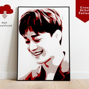 May include: A red and white cross stitch pattern of a man's face. The man is smiling and has short, dark hair. The background is white.