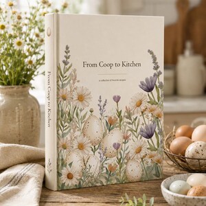 May include: A hardcover book titled From Coop to Kitchen with a cream-colored cover featuring a watercolor illustration of speckled eggs nestled among white daisies, purple lavender, and green foliage. The spine also displays the book title.
