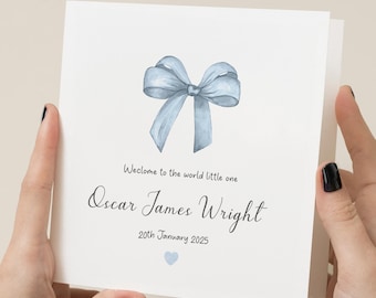 Puede incluir: Una tarjeta blanca con un lazo de acuarela azul claro en la parte superior. El texto dice "Bienvenido al mundo pequeño Oscar James Wright 20 de enero de 2025" con un pequeño corazón azul claro en la parte inferior.