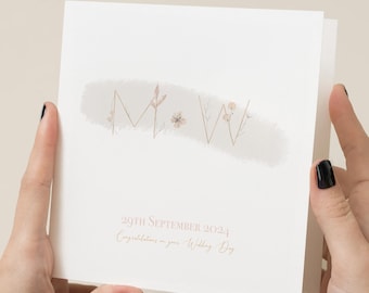 May include: A white card with a watercolor design of the letters M and W in gold with floral accents. The text "29th September 2024 Congratulations on your Wedding Day" is printed in pink at the bottom of the card.