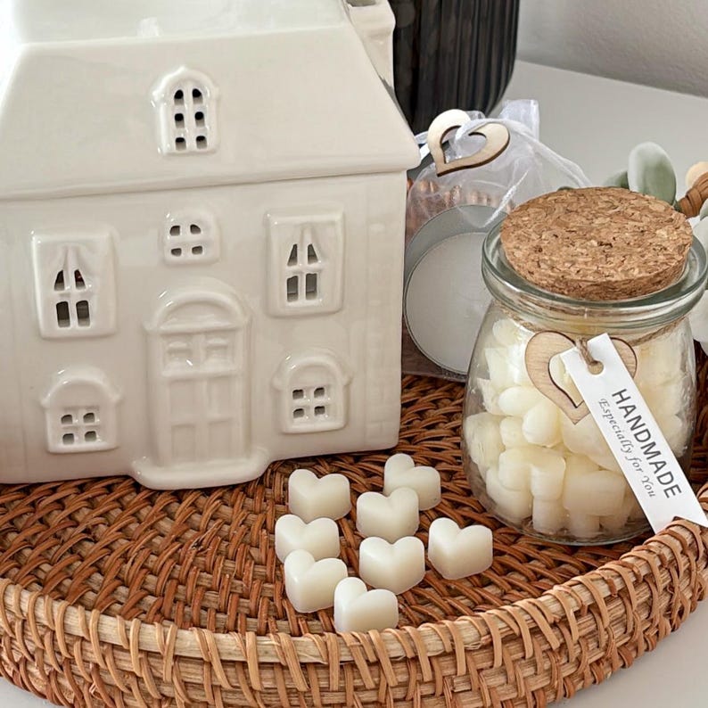 May include: A white ceramic house-shaped candle warmer with window cutouts sits on a woven tray. A glass jar with a cork lid and heart-shaped tag contains heart-shaped wax melts. The tag reads "HANDMADE, Especially for You."