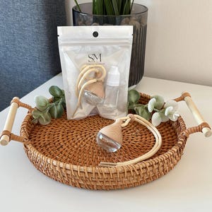 May include: Aromatherapy car diffuser set with a clear glass and wood design, displayed on a woven tray. The set includes a small bottle and a sealed package with the text "SM SCENTED MOMENTS". The tray has wooden handles.