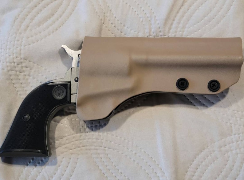 May include: A black and silver handgun with a black grip is partially inserted into a tan holster. The holster is secured with black screws. The handgun is a single-action revolver.