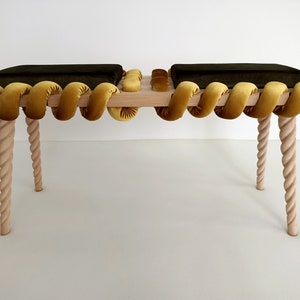 May include: A wooden bench with two dark green cushions and a yellow rope-like trim. The bench has four twisted wooden legs.