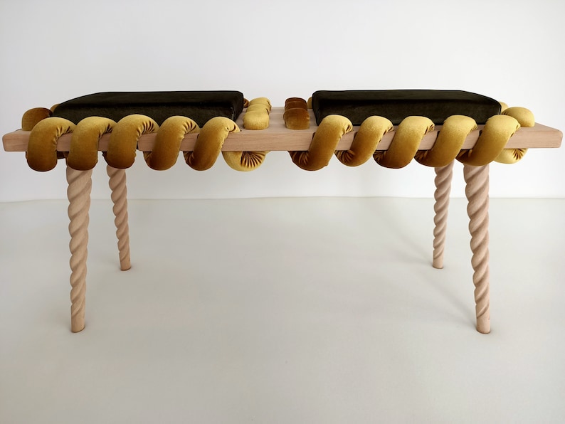 May include: A wooden bench with two dark green cushions and a yellow rope-like trim. The bench has four twisted wooden legs.