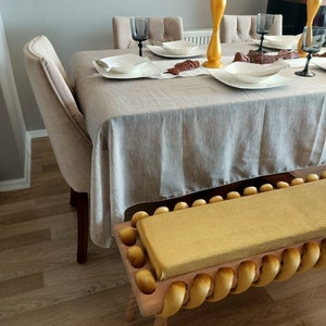 K&ouml;nnte beinhalten: Ein Esszimmer mit einem gedeckten Tisch. Der Tisch ist mit einer hellgrauen Tischdecke bedeckt und mit wei&szlig;en Tellern, Gl&auml;sern und dekorativen Gegenst&auml;nden gedeckt. Vor dem Tisch befindet sich eine gelbe Bank mit gelbem Kissen.