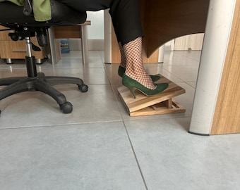 May include: A wooden footrest with two angled platforms. A person is standing on the footrest wearing green heels and black fishnet stockings.