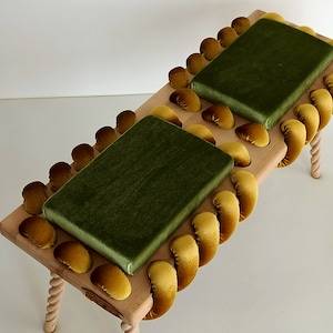 May include: A wooden bench with two green velvet cushions. The bench is decorated with a yellow velvet rope trim.