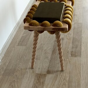 May include: A wooden bench with two dark green cushions and a gold velvet rope design. The bench has four twisted legs and a label that reads "WOOD BY RYK DESIGN".