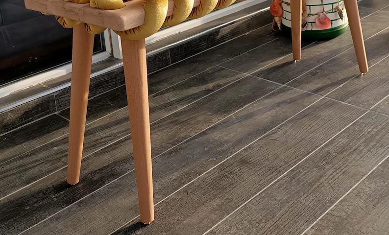 May include: A wooden bench with a yellow velvet cushion. The bench has four legs and is made of natural wood. The cushion is made of a soft, plush fabric.