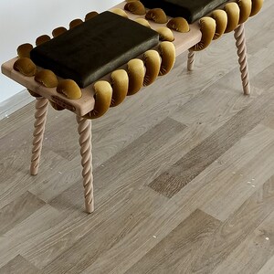 May include: A wooden bench with two dark green velvet cushions. The bench has a unique design with a rope-like border made of yellow velvet.