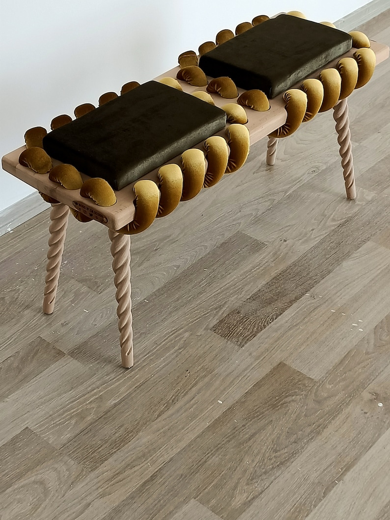 May include: A wooden bench with two dark green velvet cushions. The bench has a unique design with a rope-like border made of yellow velvet.